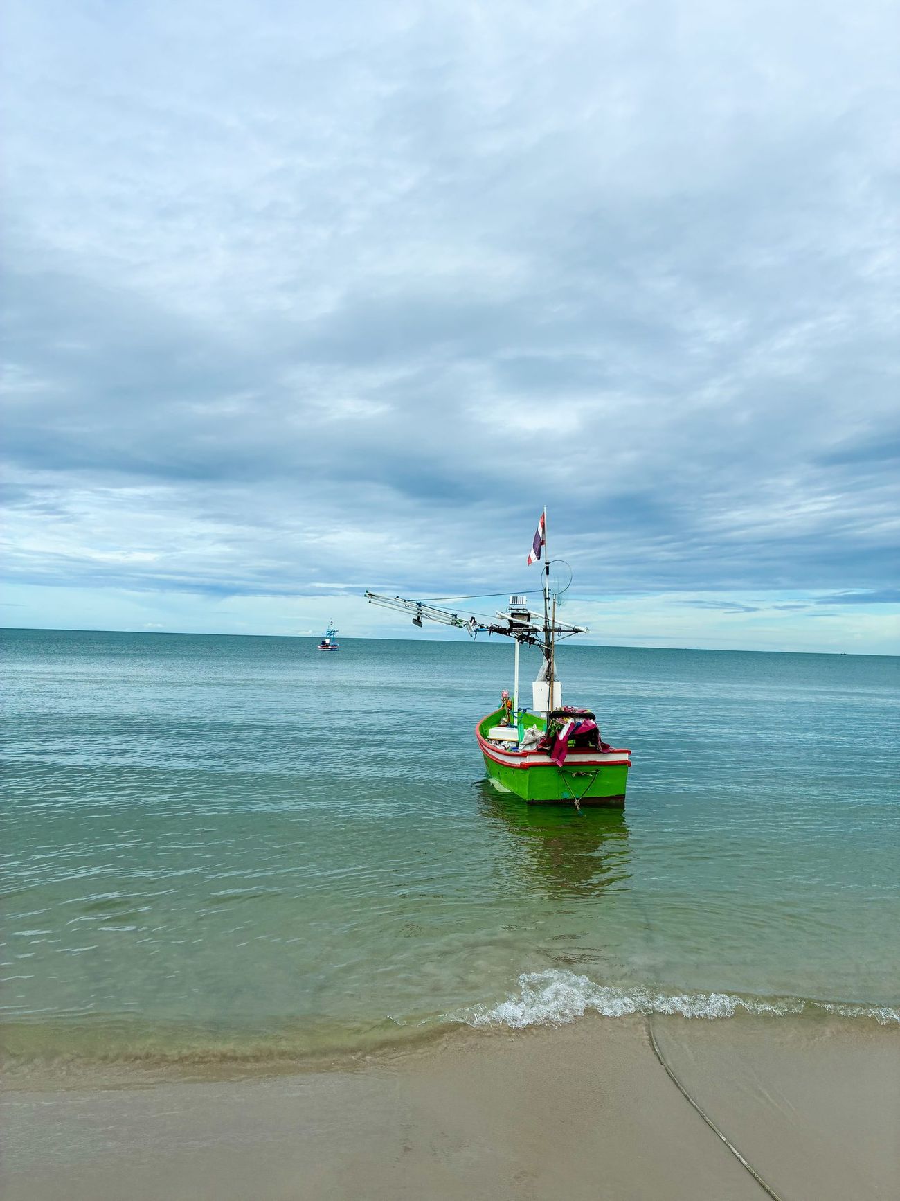 A green fishing boat on the shore at Hua Hin under a cloudy sky